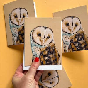 May include: A set of greeting cards featuring a hand-drawn illustration of a barn owl with a heart-shaped face, large dark eyes, and brown, white, and black plumage. The owl is depicted against a plain tan background on each card.