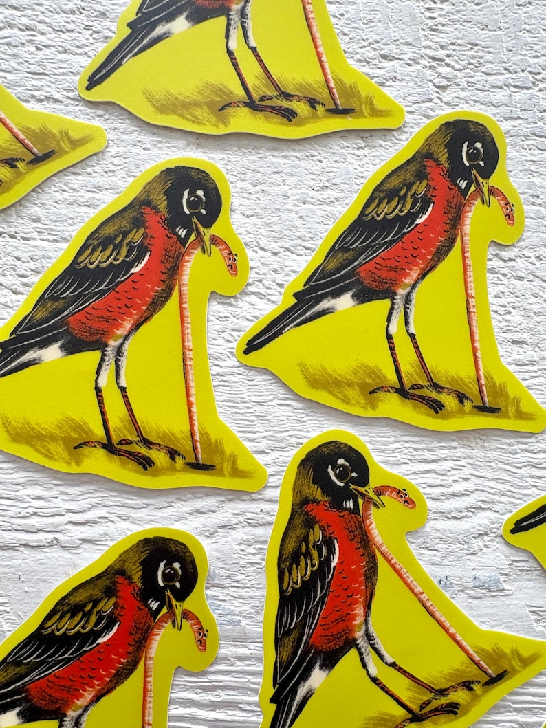 May include: Several yellow stickers featuring a stylized robin with a worm in its beak. The birds have black heads, wings, and tails, with red breasts and a long, thin worm. The stickers are on a white surface.