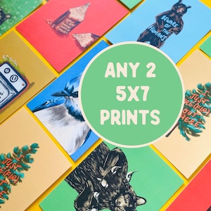 May include: A selection of 5x7 prints featuring diverse illustrations, such as a blue jay, a bear with the text "Beware of the Humans," and a pencil. The prints are displayed on a yellow backdrop, with a green circle that says "ANY 2 5X7 PRINTS."