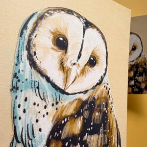 May include: A canvas print featuring a detailed illustration of a barn owl with a heart-shaped white face, large dark eyes, and brown and black speckled feathers. The owl is depicted against a light beige background with soft blue accents.