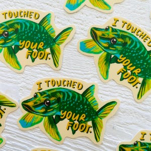 May include: Four stickers featuring a green and blue fish with the text "I Touched Your Foot." The fish has a yellow fin and a yellow tail.