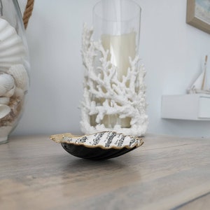May include: A black and gold seashell dish with music notes printed on the inside. The dish is sitting on a wooden surface.
