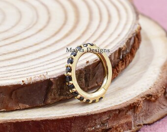 May include: A gold-colored hoop earring with a row of small black gemstones. The earring is set against a wooden background with a pink backdrop. The text "Mayla Designs" is visible on the wood.