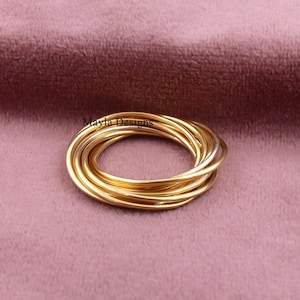 May include: A gold-colored multi-band ring consisting of several thin, interlocking circular wires that form a single cohesive piece. The ring features the text Mayla Designs printed in small black letters near the top of the metal bands.