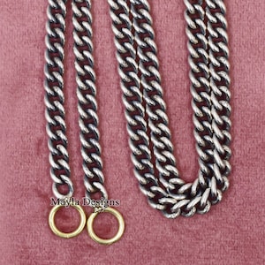 Könnte beinhalten: Silberfarbene Kette mit großen, ineinandergreifenden Gliedern. Die Kette hat unten zwei goldfarbene Ringe. Die Kette wird auf einem rosa Hintergrund präsentiert. Der Text "Mayla Designs" ist in der Nähe der Ringe zu sehen.