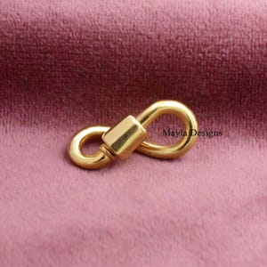May include: A gold-toned metal lobster clasp with a smooth, polished finish and a central rectangular connector. The clasp features two rounded loops on either side of the central mechanism, with the text Mayla Designs printed clearly nearby.