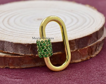 Könnte beinhalten: Goldene ovale Karabinerverschluss mit einem grünen, mit Kristallen besetzten Zylinder. Mayla Designs ist auf der Holzoberfläche aufgedruckt.