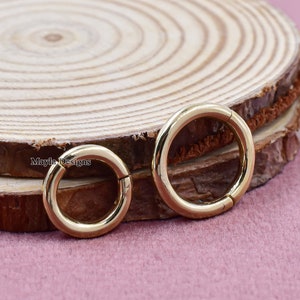 May include: Two gold hoop earrings with a hinged closure. The earrings are on a wooden surface.