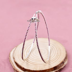 Puede incluir: Pendientes de aro de plata con una fila de pequeñas piedras preciosas rosas alrededor del borde.