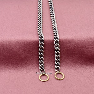 Puede incluir: Dos cadenas de plata con anillos de salto de oro en los extremos. Las cadenas están sobre un fondo rosa.