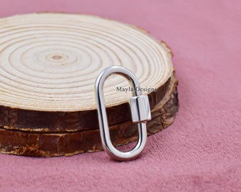 May include: Silver oval-shaped lobster clasp with a cylindrical trigger. The clasp is on a wooden surface.