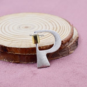 Op de afbeelding: Zilveren letter 'P' bedel met een gouden accent. De bedel ligt op een houten oppervlak.