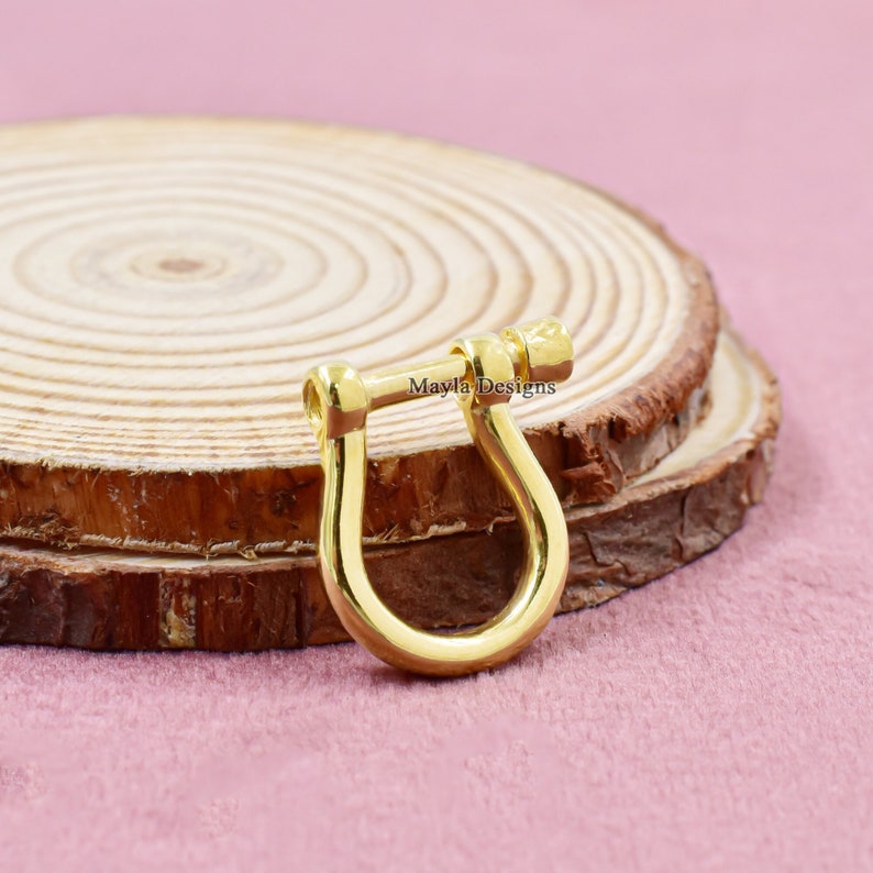 Pode incluir: Fecho em forma de U de metal dourado com fecho de parafuso. O fecho est&aacute; sobre uma superf&iacute;cie de madeira.
