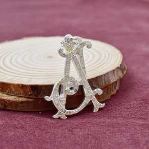 May include: A silver pendant in the shape of the letter A, encrusted with small, clear diamonds. The pendant is on a wooden surface.