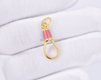 Pode incluir: Encanto de metal dourado com um acento de esmalte rosa. O encanto apresenta um laço em uma extremidade e um gancho na outra.