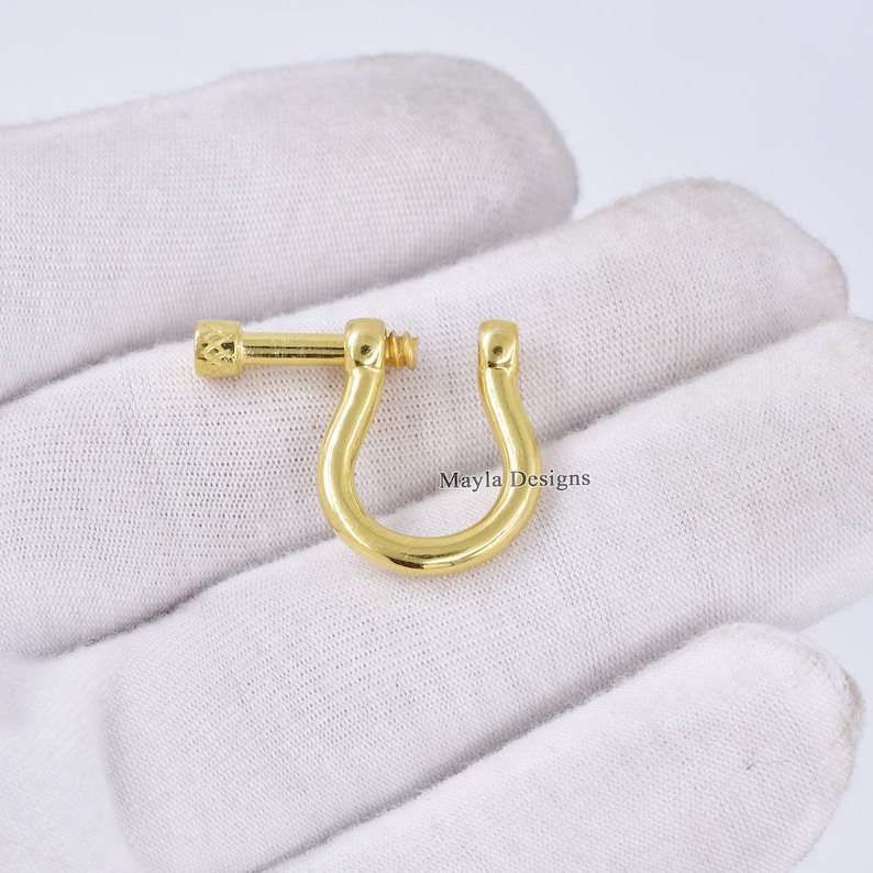 Pode incluir: Fecho girat&oacute;rio de metal dourado com fecho de parafuso. O fecho tem a forma de uma ferradura e tem um acabamento liso e polido.