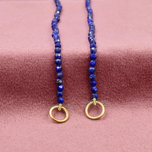 Pu&ograve; includere: Due fili di perline sfaccettate di lapislazzuli blu intenso con chiusure circolari color oro. Le perline sono infilate insieme, creando un design delicato ed elegante. Il testo "Mayla Designs" &egrave; visibile sulle chiusure.