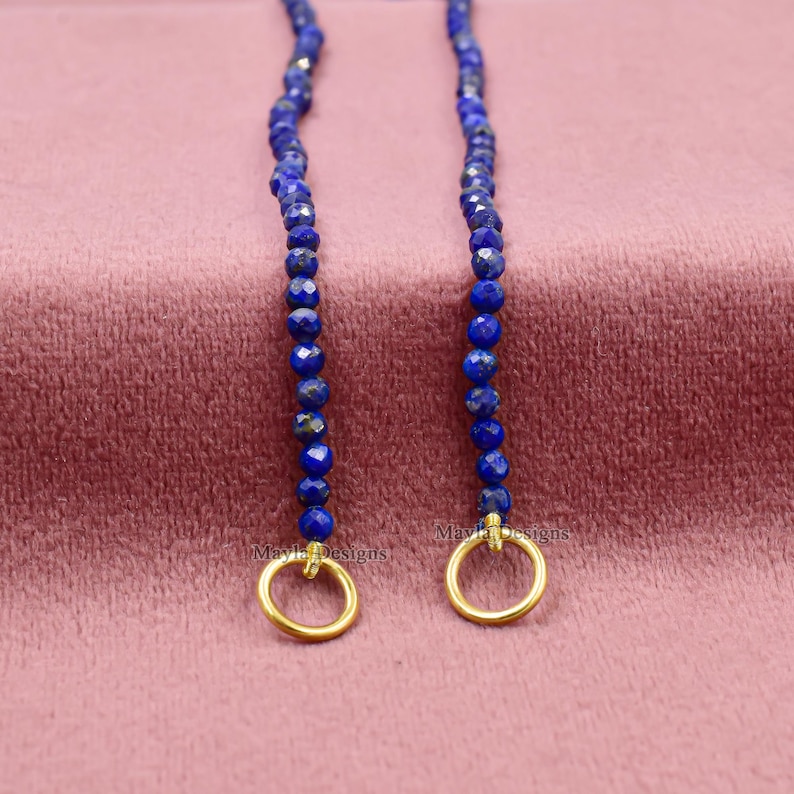 Pu&ograve; includere: Due fili di perline sfaccettate di lapislazzuli blu intenso con chiusure circolari color oro. Le perline sono infilate insieme, creando un design delicato ed elegante. Il testo "Mayla Designs" &egrave; visibile sulle chiusure.