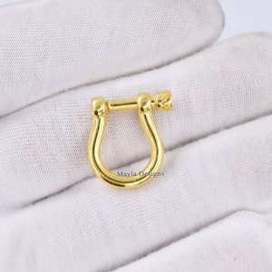 Pode incluir: Fecho girat&oacute;rio de metal dourado com uma pega texturizada. O fecho tem a forma de uma ferradura com uma abertura arredondada.