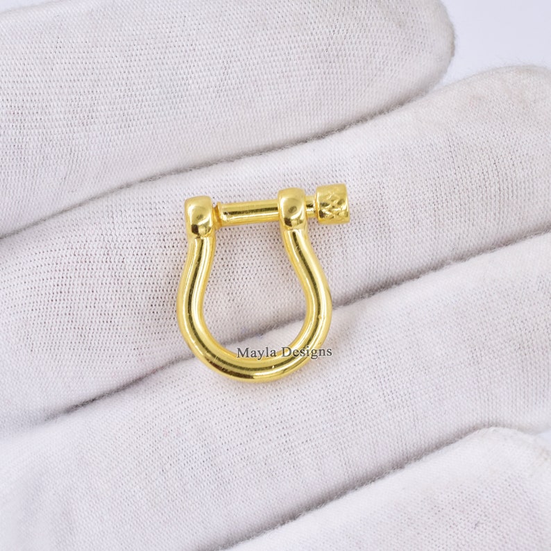 Pode incluir: Fecho girat&oacute;rio de metal dourado com uma pega texturizada. O fecho tem a forma de uma ferradura com uma abertura arredondada.
