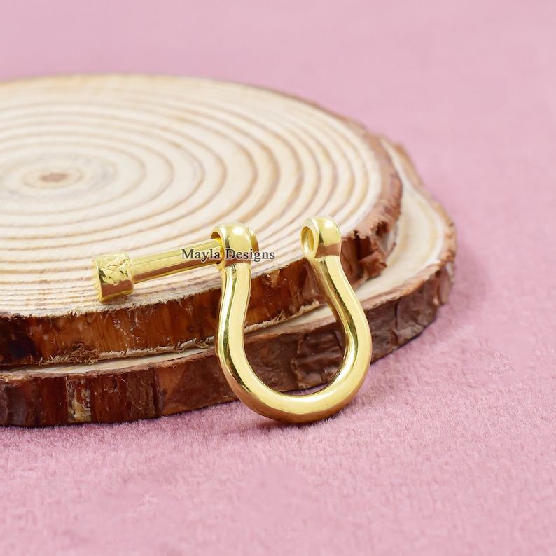 Pode incluir: Fecho de metal dourado com um design em forma de U. O fecho est&aacute; sobre uma superf&iacute;cie de madeira. Mayla Designs est&aacute; escrito na superf&iacute;cie.