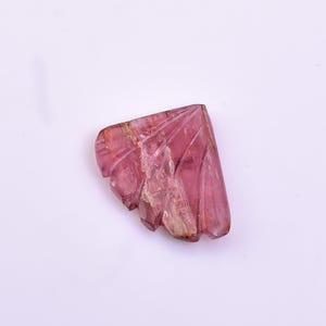 May include: A carved pink tourmaline gemstone with a unique, fan-shaped design. The gemstone has a translucent appearance and exhibits a variety of pink hues.