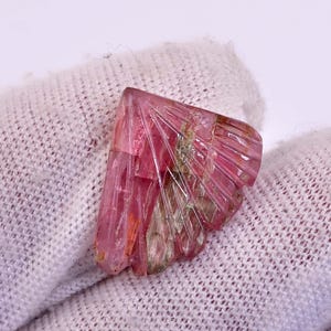 May include: A pink and green gemstone with a fan-shaped pattern. The gemstone is cut and polished, and it has a translucent appearance.
