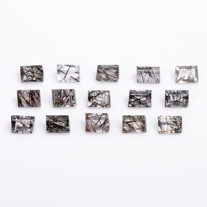 May include: A collection of 15 clear quartz gemstones with black inclusions. The gemstones are rectangular in shape and have a smooth, polished finish.
