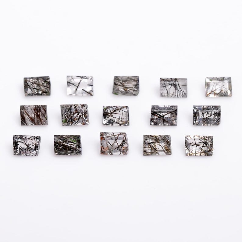 May include: A collection of 15 clear quartz gemstones with black inclusions. The gemstones are rectangular in shape and have a smooth, polished finish.