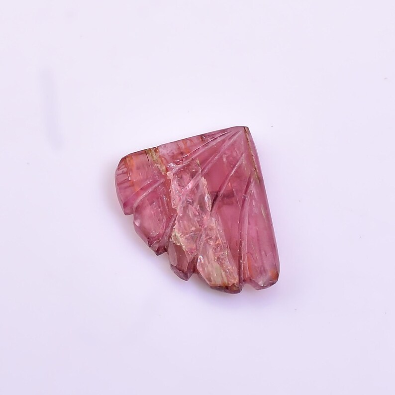 May include: A carved pink tourmaline gemstone with a unique, fan-shaped design. The gemstone has a translucent appearance and exhibits a variety of pink hues.