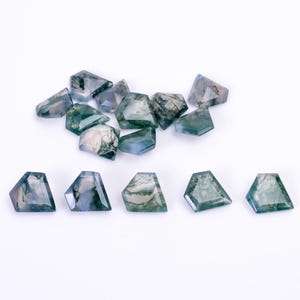 May include: A collection of loose moss agate gemstones, each cut into a faceted trapezoidal shape. The stones display translucent to opaque surfaces with characteristic dark green, fern-like dendritic inclusions set against a pale background.