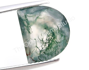 以下が含まれることがあります： 白い背景に緑色のモスマラカイトのcabochon。樹枝状の模様が入っています。石は楕円形で、滑らかで磨かれた表面をしています。