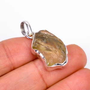 Puede incluir: Un colgante de plata con una piedra preciosa en bruto de color marrón claro y verde, de forma irregular y texturada.