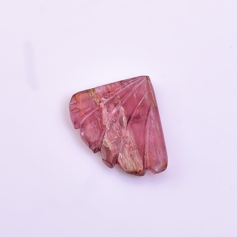 May include: A carved pink tourmaline gemstone with a unique, fan-shaped design. The gemstone has a translucent appearance and exhibits a variety of pink hues.