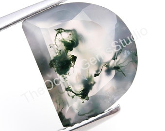 以下が含まれることがあります： 白い背景に緑色のモスアゲートのcabochon。石には、緑色の苔のようなインクルージョンが渦巻く独特のパターンがあります。