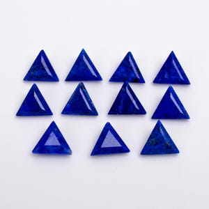 Könnte beinhalten: Zwölf dreieckige Lapislazuli-Edelsteine. Die Edelsteine sind tiefblau und haben eine polierte Oberfläche.