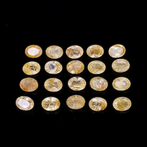 Può includere: Una collezione di gemme taglio ovale, di colore giallo dorato, con inclusioni interne a forma di ago. Le gemme sono disposte in file su sfondo nero, mettendo in risalto le loro superfici lucide e i motivi naturali. Adatte per la creazione di gioielli.