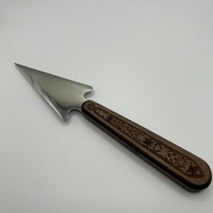 May include: A silver spearhead with a wooden handle featuring a carved design. The handle is brown with a dark wood grain.