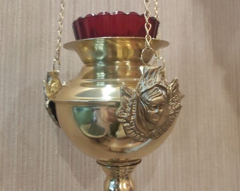 May include: A gold hanging oil lamp with a red glass shade and a decorative angel figure on the side.