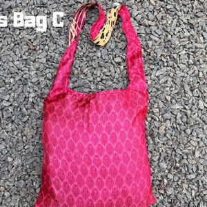 Pu&ograve; includere: Una borsa a tracolla rosa acceso con un motivo a foglie ripetuto. La borsa ha lunghe cinghie e il testo "Cross Bag C" nell'angolo in alto a sinistra. Il cinturino ha un design giallo e rosa.