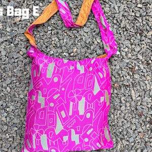 Pu&ograve; includere: Una borsa a tracolla rosa acceso con un motivo astratto ripetuto in argento. La borsa ha una tracolla rosa abbinata e una tracolla arancione a contrasto. Il testo "Cross Bag E" &egrave; nell'angolo in alto a sinistra.