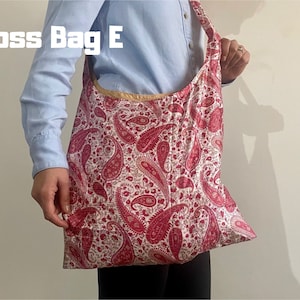 Pu&ograve; includere: Una grande borsa tote con un motivo paisley rosso e bianco. La borsa ha un'ampia tracolla e un bordo color oro. Il testo "Cross Bag E" &egrave; stampato in lettere bianche nell'angolo in alto a sinistra.