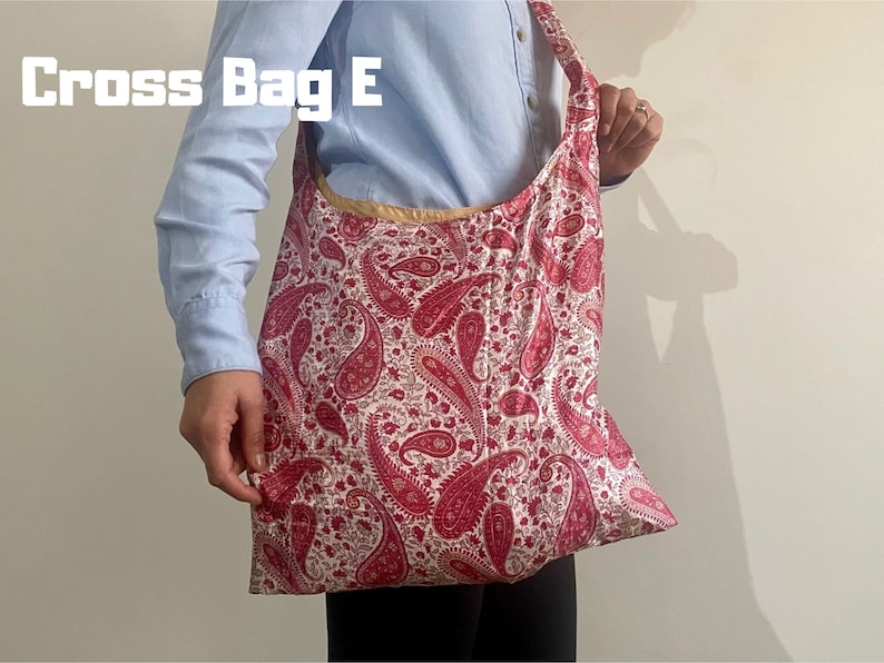 Pu&ograve; includere: Una grande borsa tote con un motivo paisley rosso e bianco. La borsa ha un'ampia tracolla e un bordo color oro. Il testo "Cross Bag E" &egrave; stampato in lettere bianche nell'angolo in alto a sinistra.