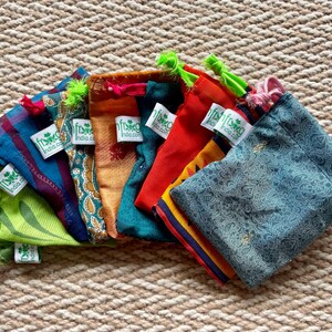 Pu&ograve; includere: Assortimento di sacchetti in tessuto con coulisse di diversi colori con un logo a foglia verde e il testo "fishka india.com".