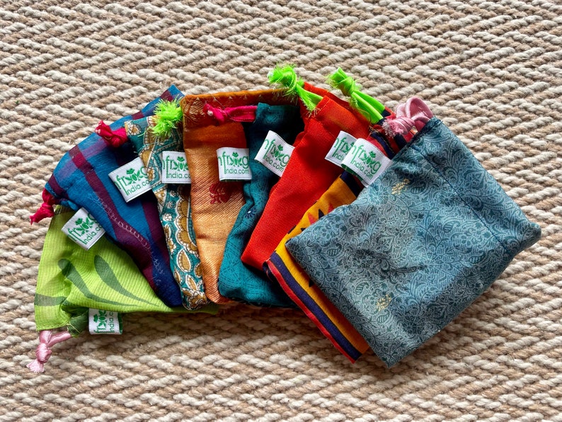 Pu&ograve; includere: Assortimento di sacchetti in tessuto con coulisse di diversi colori con un logo a foglia verde e il testo "fishka india.com".