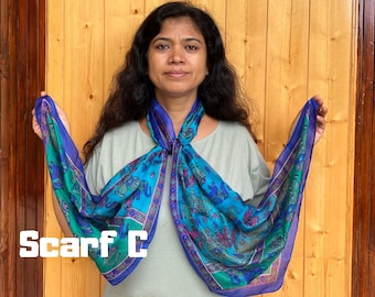 May include: A rectangular scarf featuring a vibrant blue and green color palette with a repeating pattern of elephants in shades of pink, purple, and teal. The scarf has a dark blue border and the text Scarf C is printed in white.