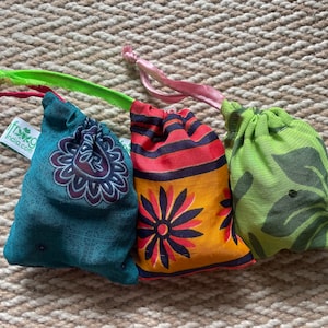 May include: Three small drawstring bags made of fabric with different patterns. The bags are green, blue, and orange with floral and leaf designs. The bags have a green, pink, and red drawstring.