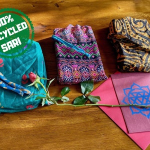 Pu&ograve; includere: Tre pochette in tessuto realizzate con tessuto sari riciclato al 100%. Le pochette sono di colori e motivi diversi. Un'unica rosa rossa &egrave; appoggiata sulle pochette.