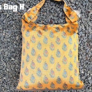 Pu&ograve; includere: Una borsa a tracolla gialla con un motivo floreale blu, rosso e bianco. La borsa ha una forma quadrata e un cinturino abbinato. Il testo "Cross Bag H" si trova nell'angolo in alto a sinistra.