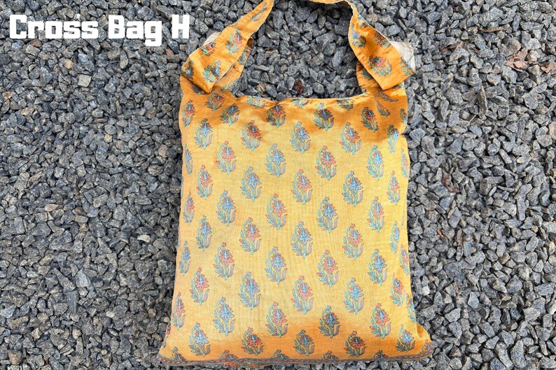 Pu&ograve; includere: Una borsa a tracolla gialla con un motivo floreale blu, rosso e bianco. La borsa ha una forma quadrata e un cinturino abbinato. Il testo "Cross Bag H" si trova nell'angolo in alto a sinistra.